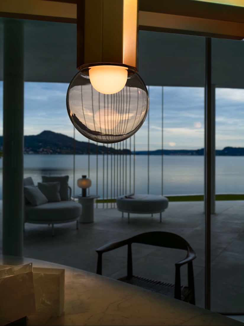 Brokis Prisma Single Pendant Large 500 glows in a minimalist room with lake views, lounge chairs, and mountains at twilight.