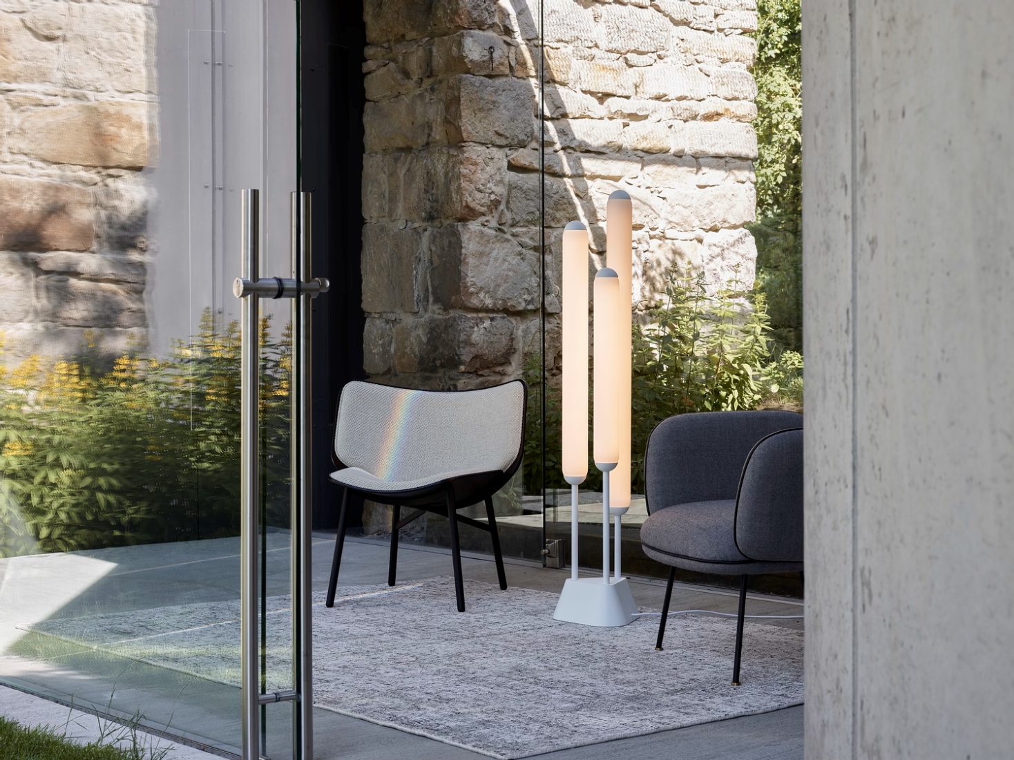 A luxurious seating area with Brokis Puro Floor 3 Tubes 1350, modern chairs, sun-cast rainbow, and garden views.