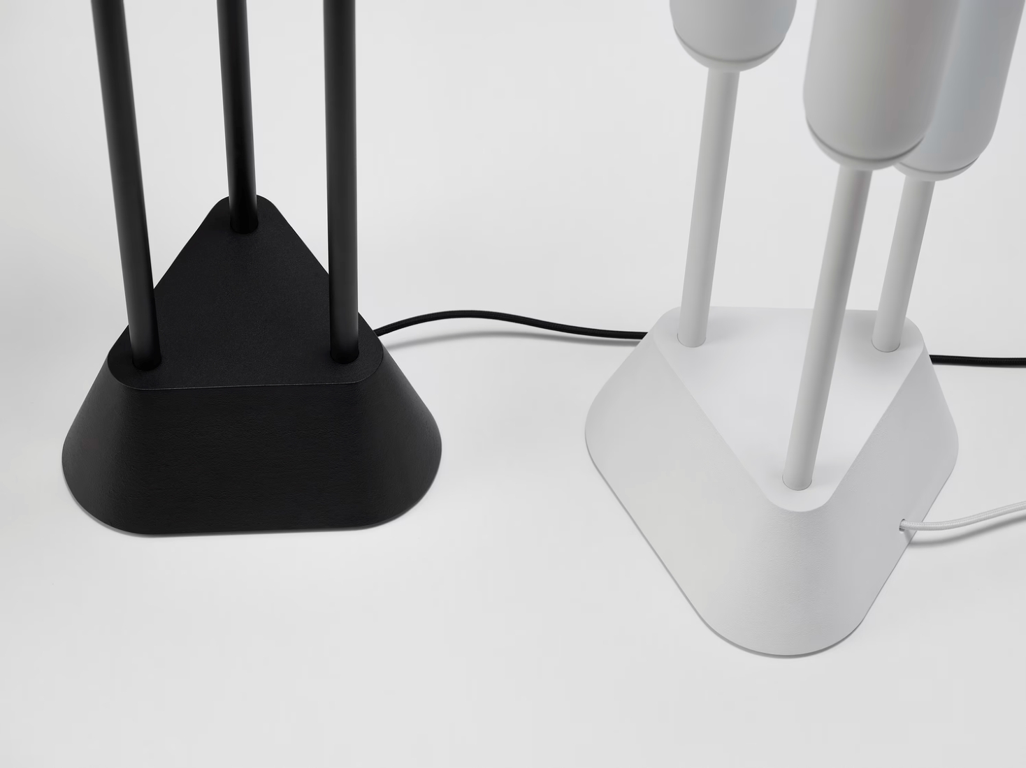 Two Brokis Puro Floor triangular bases, one black and one white, with artful flexes crossing atop a pristine white surface.