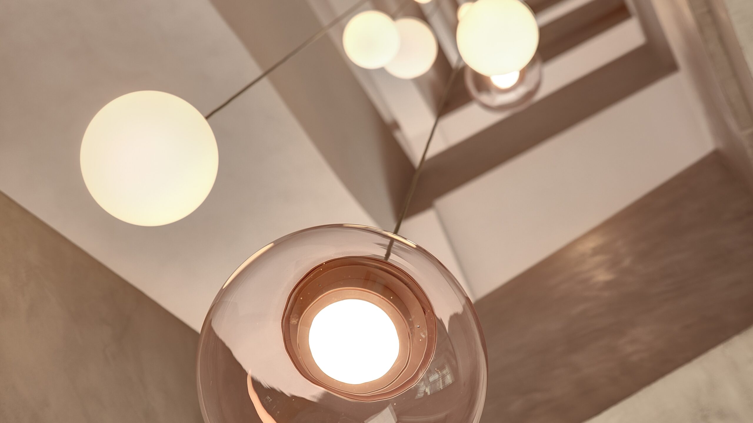 Brokis Sfera pendants in an upward view of spheres suspended in a vertical line amid angular beige staircase.