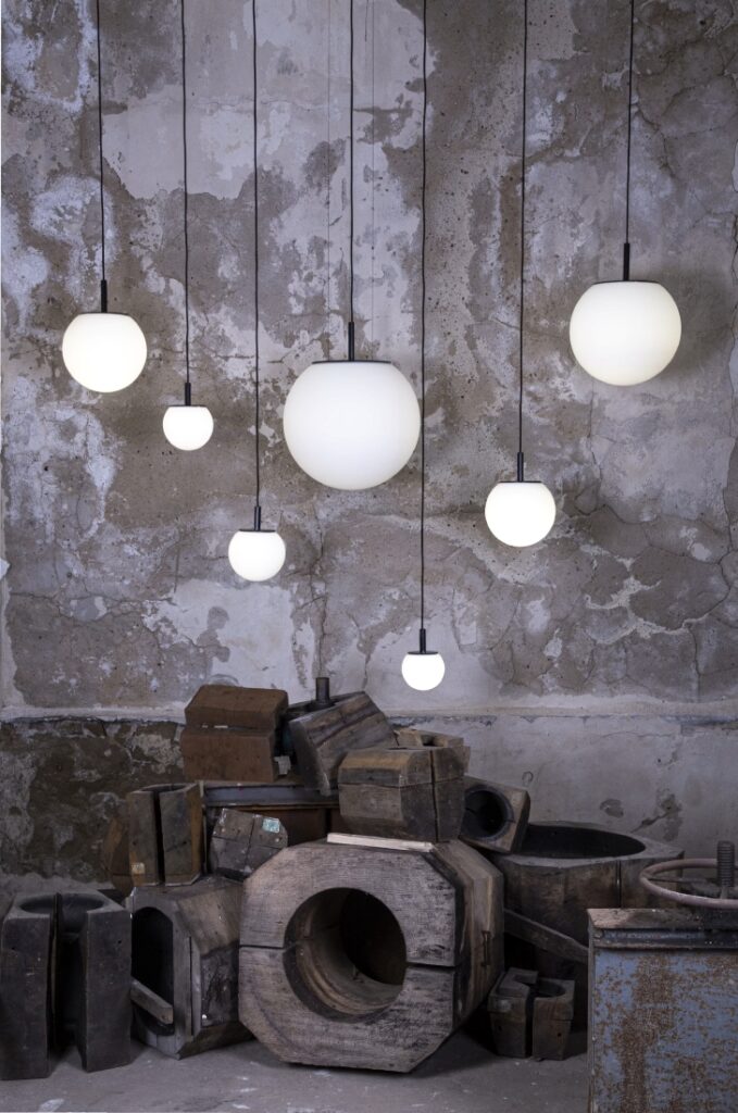 Brokis Sfera pendants float before a textured concrete wall above stacked vintage wooden industrial moulds.