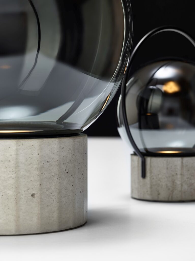 Two Brokis Sfera Portable lamps with handblown glass domes and concrete bases glow elegantly in a dark backdrop.