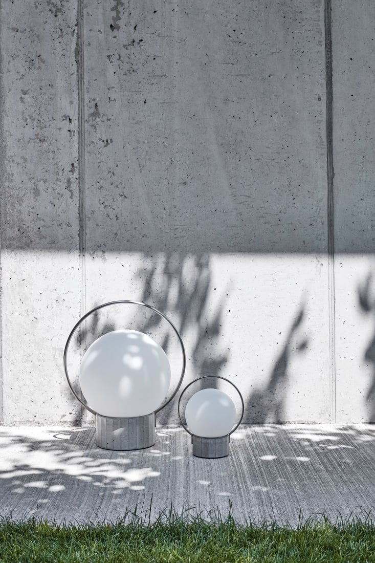 Brokis Sfera Portable lamps with slim black handles rest on concrete; dappled sun and tree shadows evoke refined ambience.