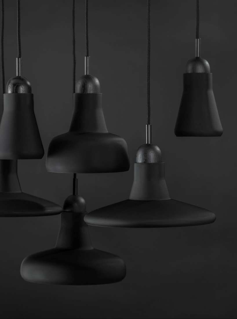 Six matte black Brokis Shadows pendants in sculptural geometric forms cluster elegantly against a moody, monochrome backdrop.