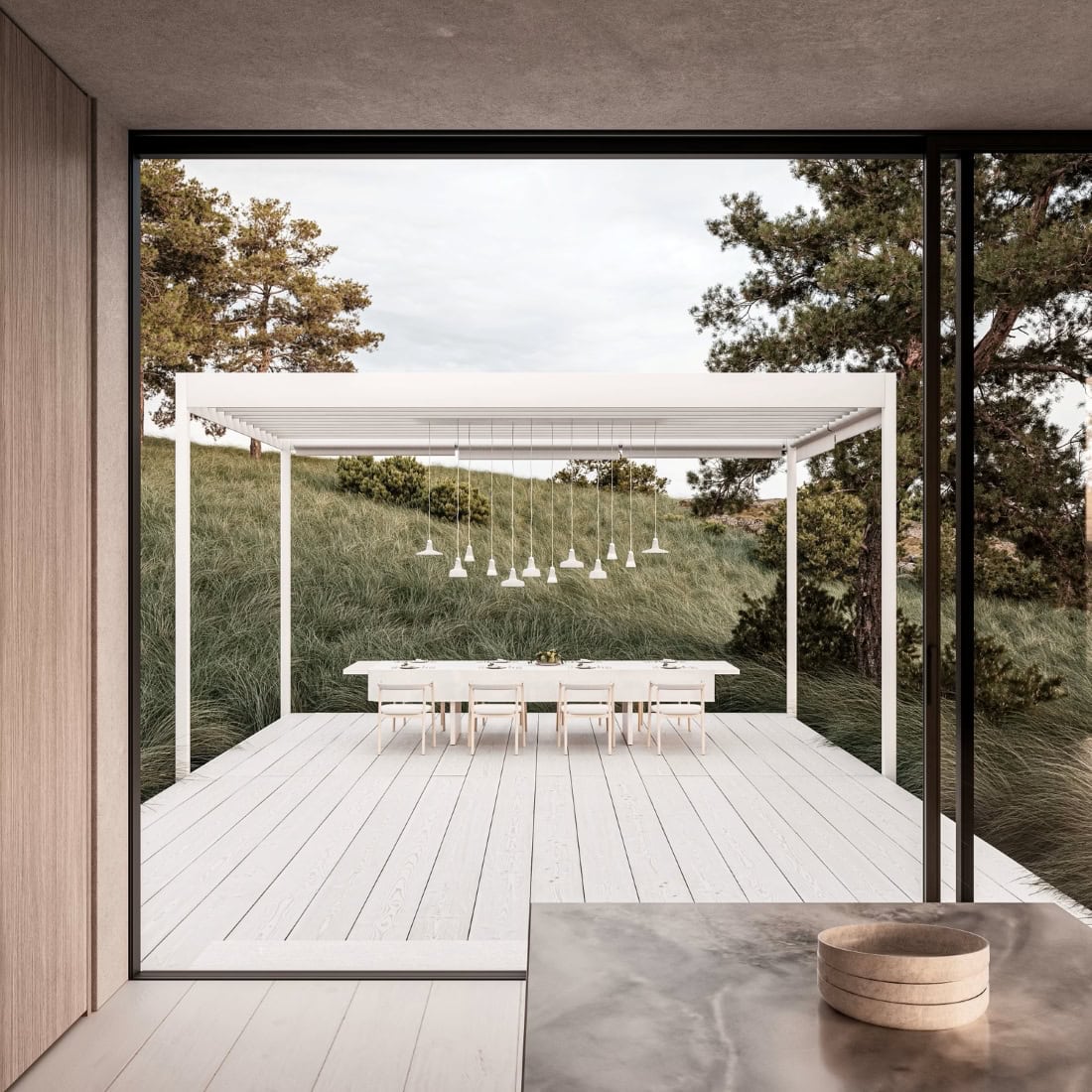 Outdoor dining on a white deck, seen through glass doors, with Brokis Shadows Exterior pendants beneath a pergola.