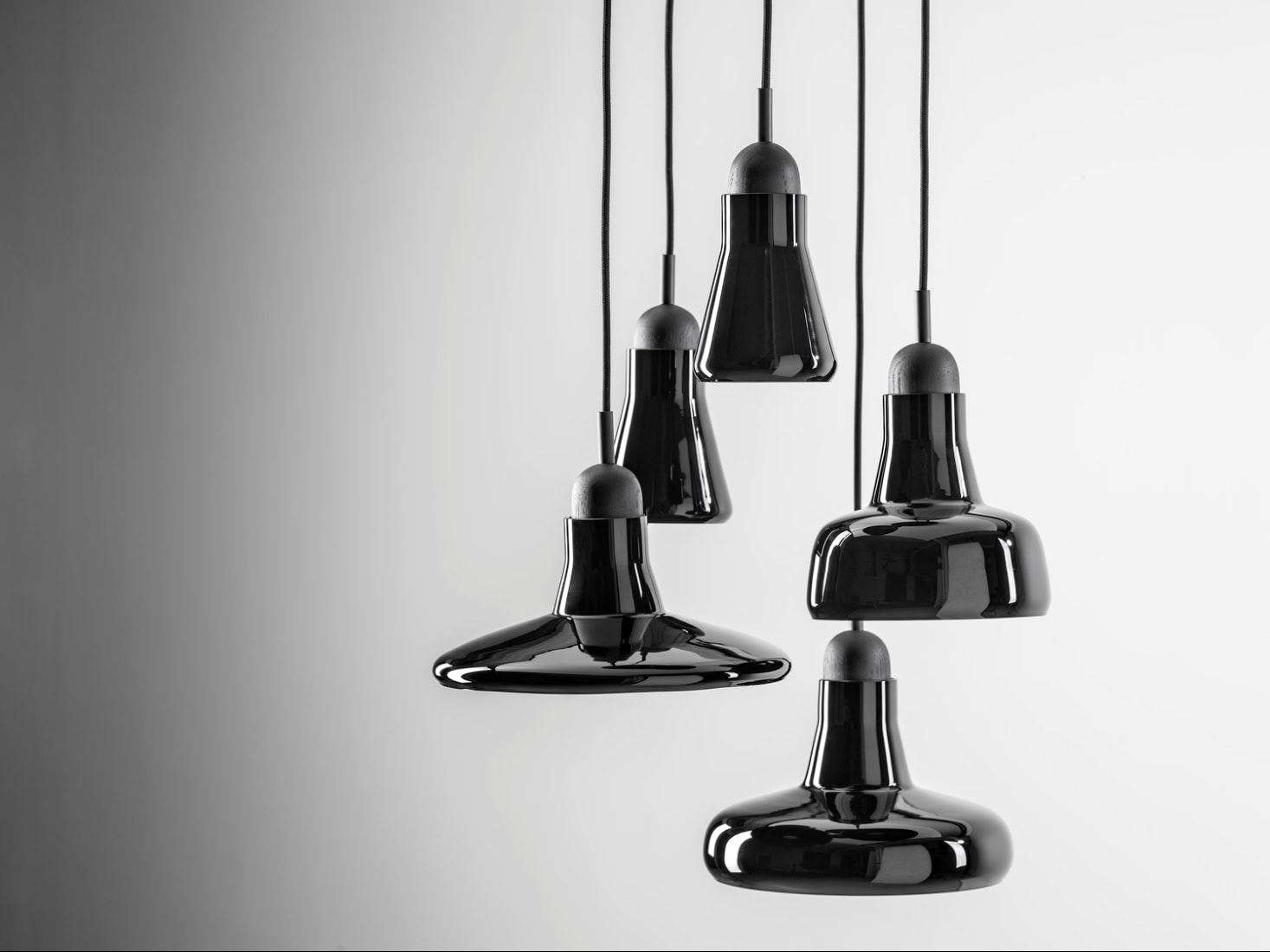 Five black Brokis Shadows pendants hang at varying heights against a chic gradient grey backdrop.