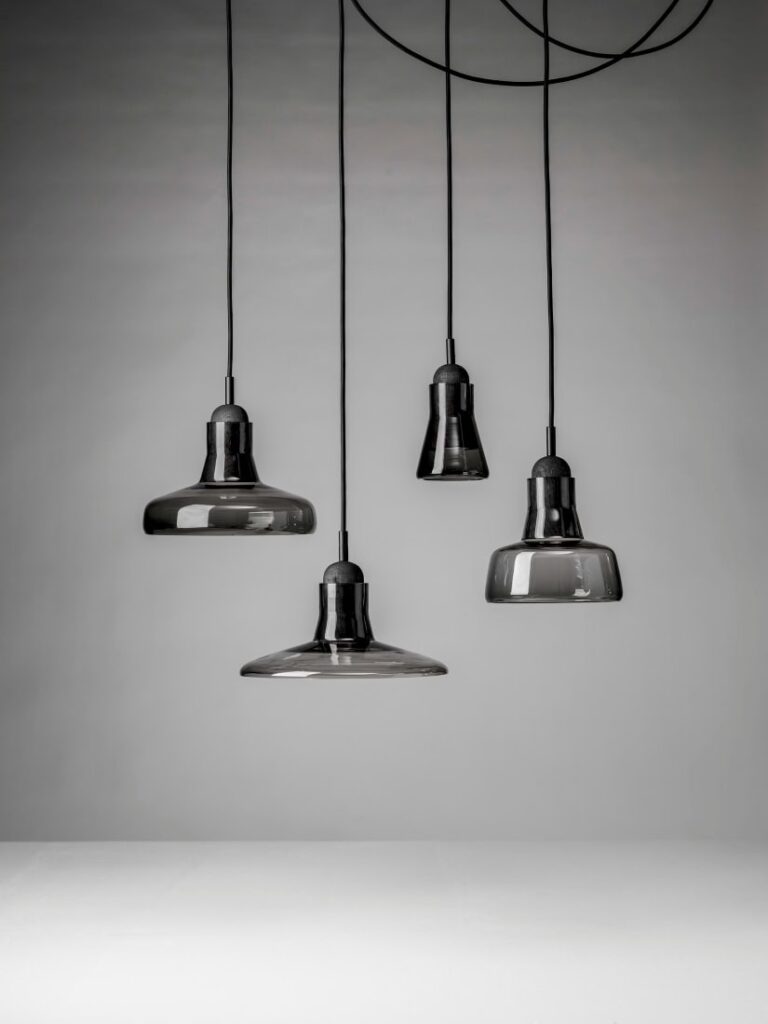 Four Brokis Shadows pendants in hand-blown glass hang at varied heights, illuminating a sleek, minimal white surface.