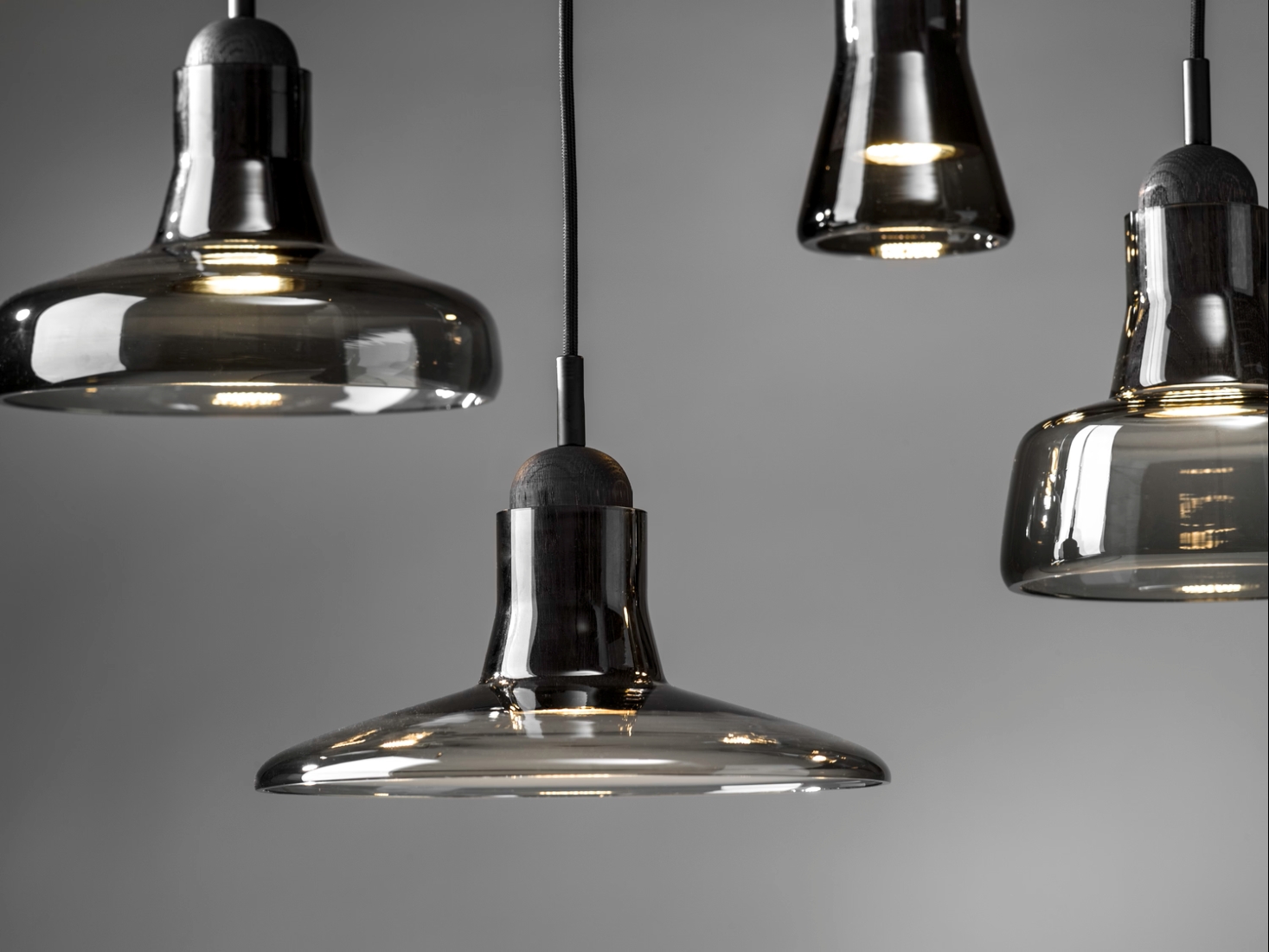 Four Brokis Shadows pendants in smoke grey glass emit a warm glow, reflecting modern luxury against grey.