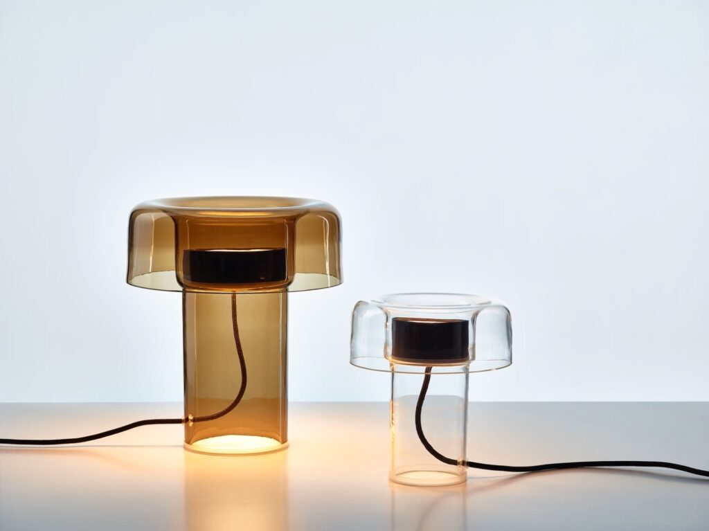 Two Brokis Spectra glass lamps - one brown, one clear - boast handblown cylindrical bases and bold black light circles.