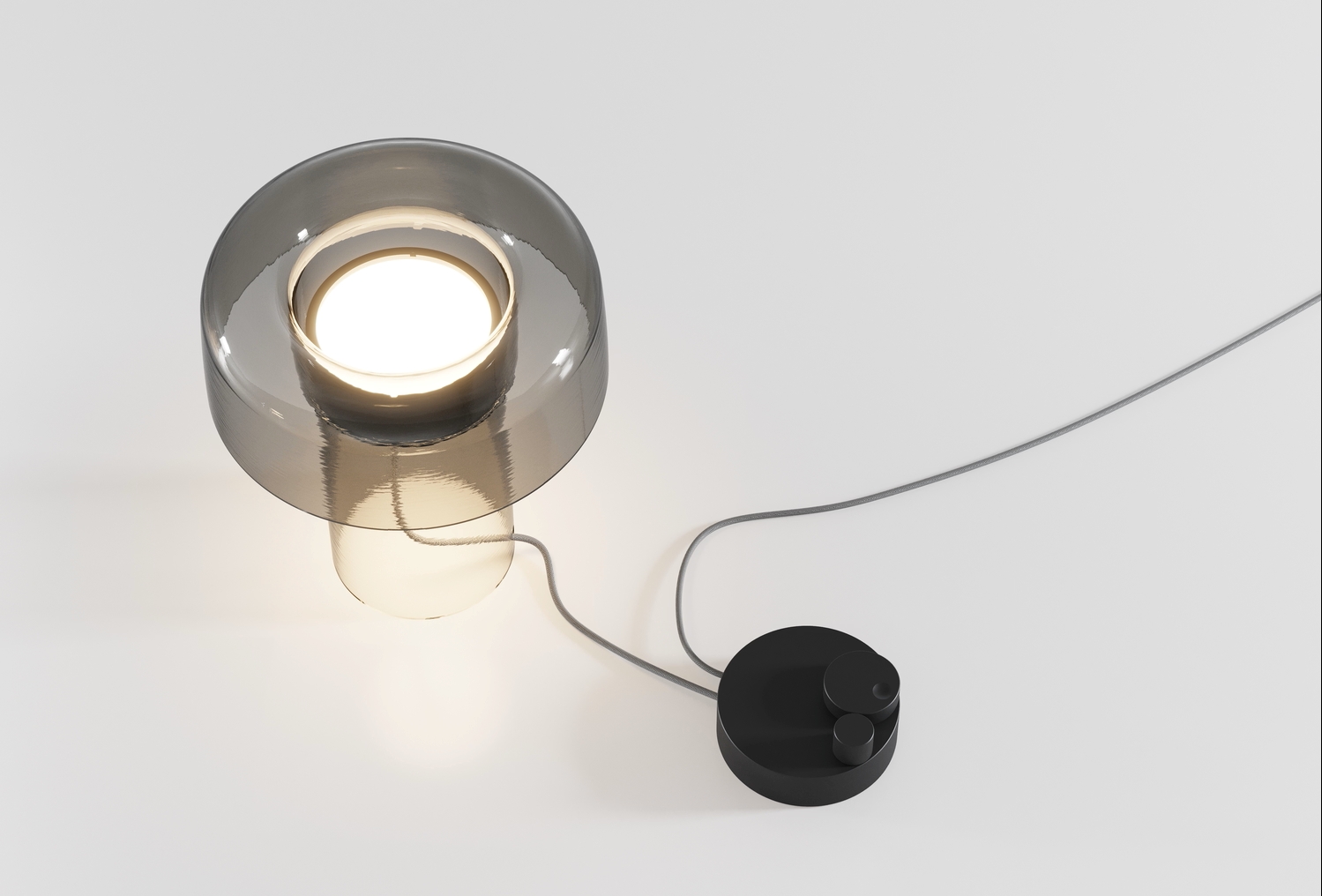 Brokis Spectra Mini Table lamp with a grey glass shade glows atop a white surface; minimal and elegant design.