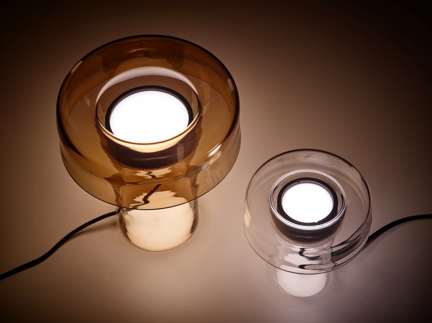 Brokis Spectra Table lamps with handblown brown and clear glass shades emit a gentle white glow on a luxe surface.