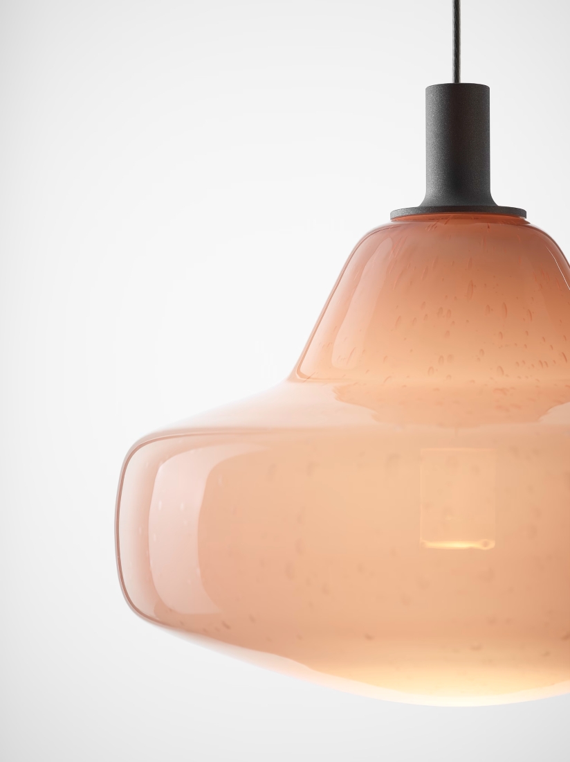 A close-up of a Brokis Starcloud Atria Pendant with handblown pink glass, softly glowing from a slim, dark metal fitting.