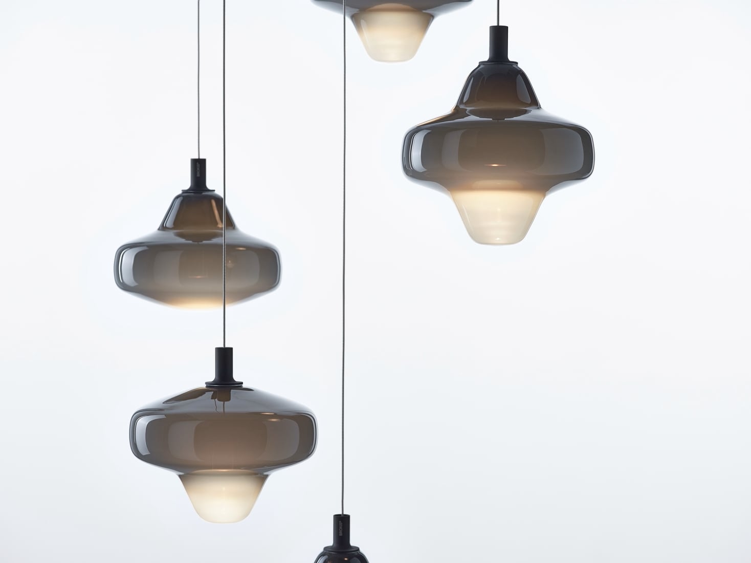 Brokis Starcloud Pendants in sculptural forms hang at varied heights, casting a warm glow over a white backdrop.