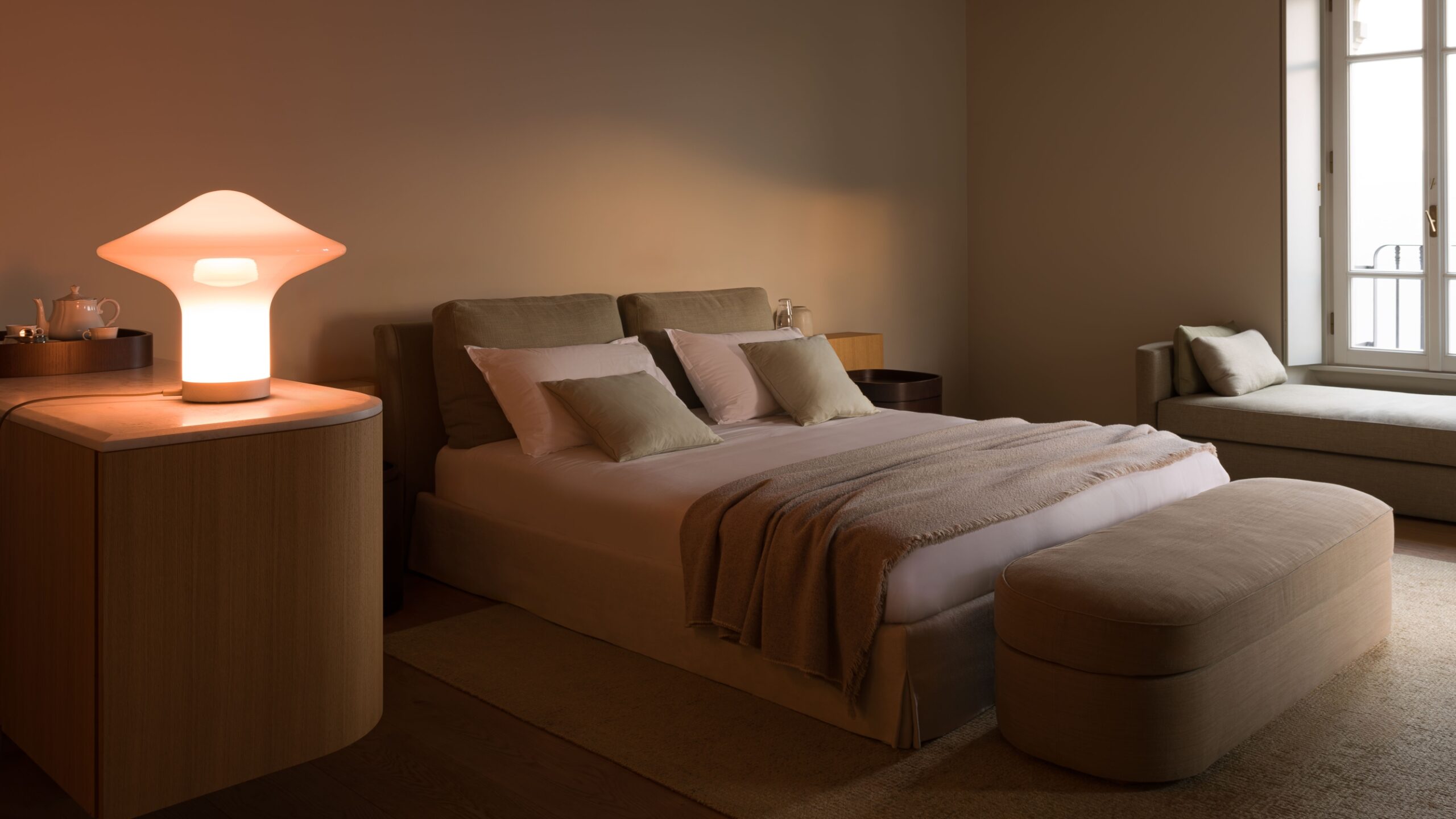Brokis Trottola Table L aglow on a sleek wood bedside table in a serene bedroom with a double bed and plush beige bedding.