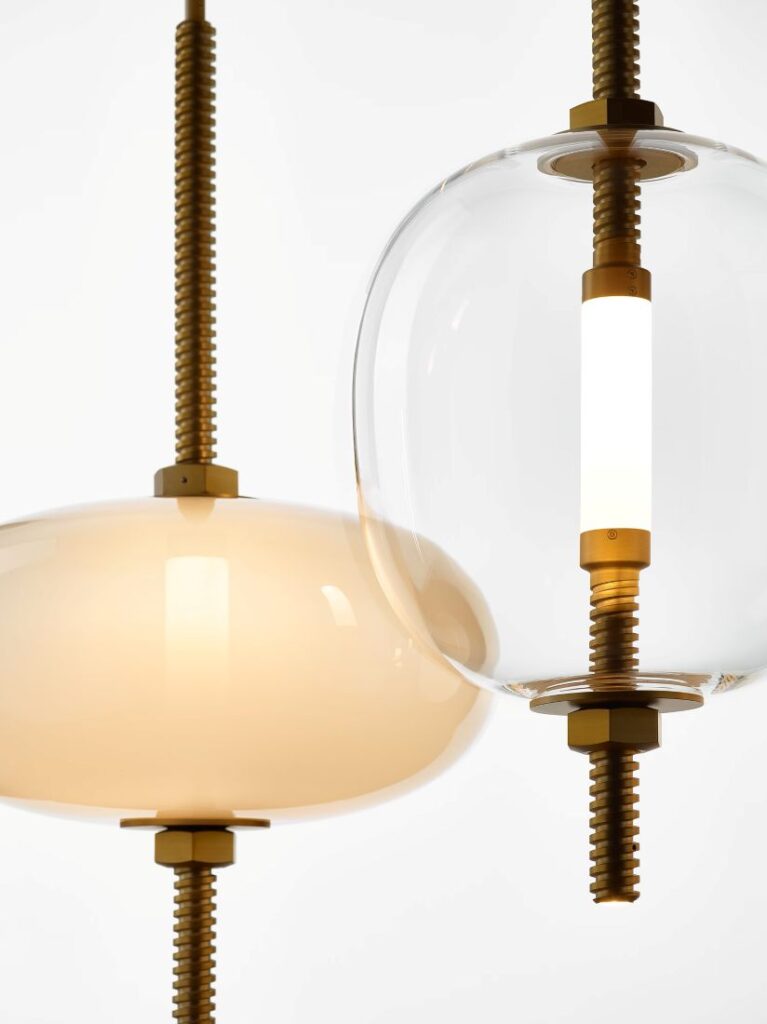 Brokis Under Pressure pendants with glass domes on brass rods; one opaline, one clear, set against a pristine white backdrop.