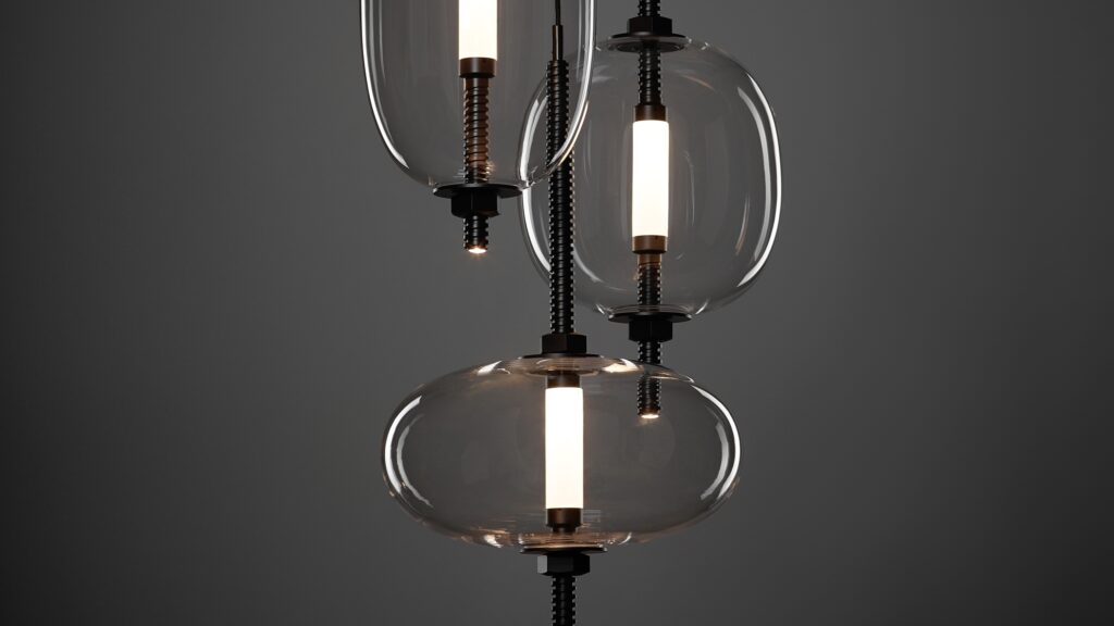 Three Brokis Under Pressure pendants with handblown glass shades and metal accents hang against a dark grey backdrop.