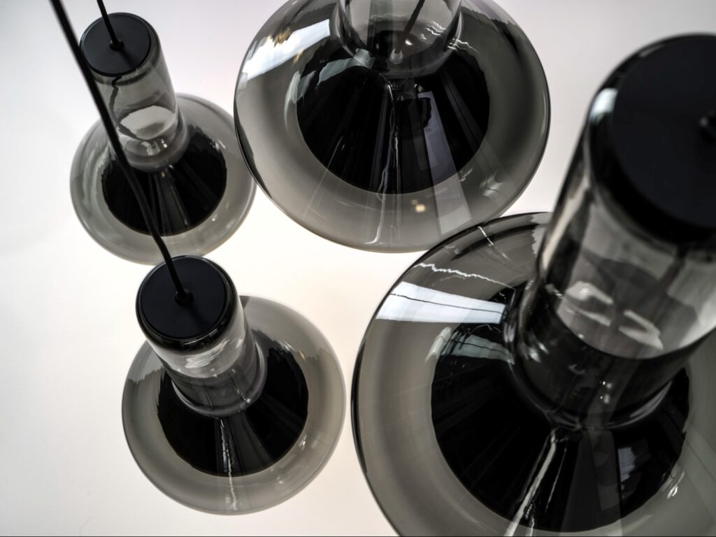 Top-down close-up of four Brokis Whistle pendants with smoke grey glass, luminous on a white backdrop.