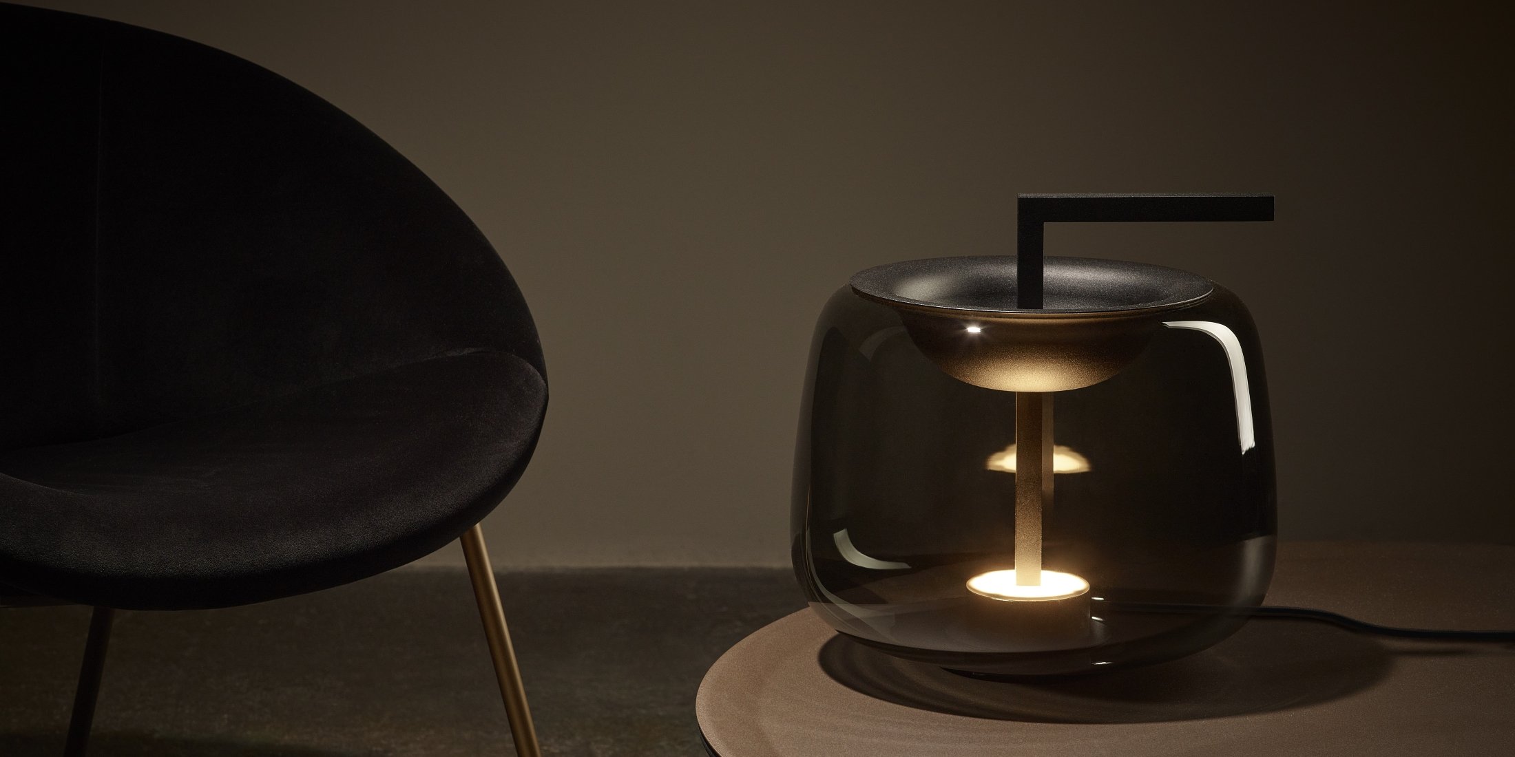 Brokis Double Table lamp next to a black velvet chair with gold legs beside a round table.