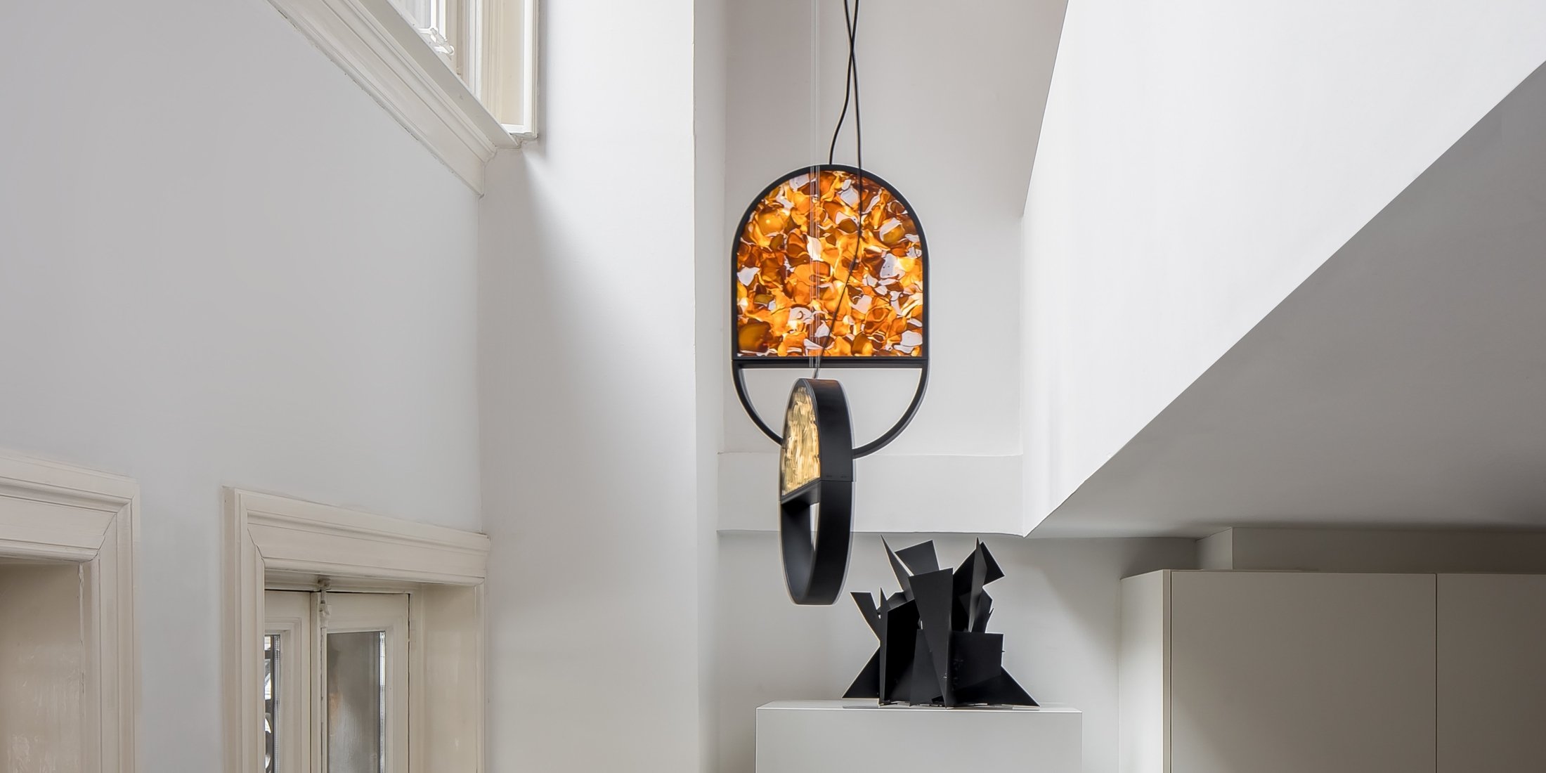 Brokis Geometric pendant in a modern space with white walls, above an abstract sculpture, autumn leaves outside.