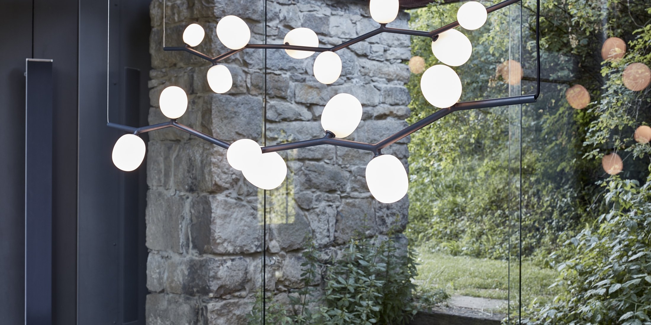 Brokis Ivy Horizontal Chandeliers with branches and glass orbs graces a rustic stone wall by a grand window.