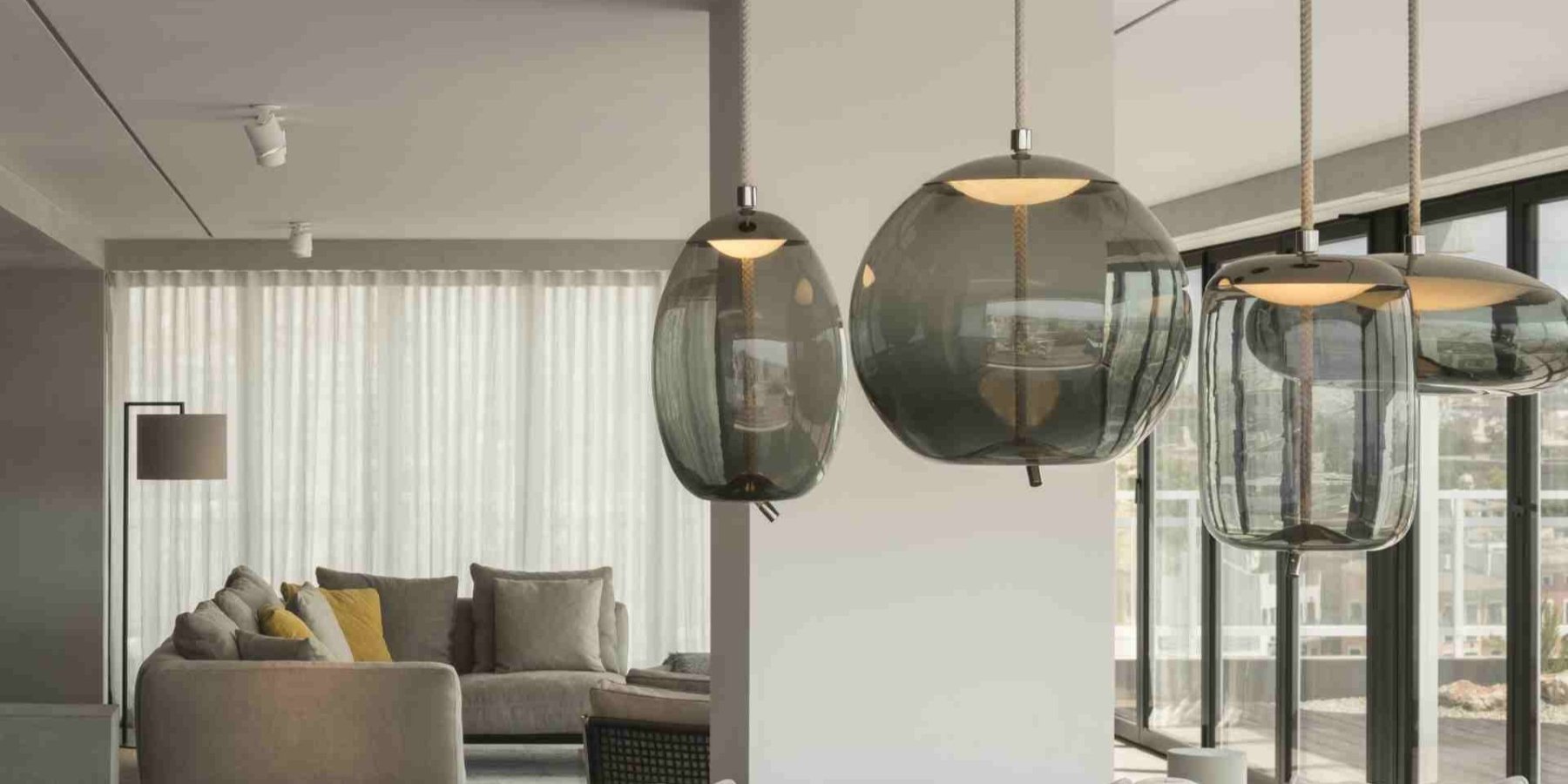 Brokis Knot pendants accent a sunlit living room with sheer curtains and a beige sofa.