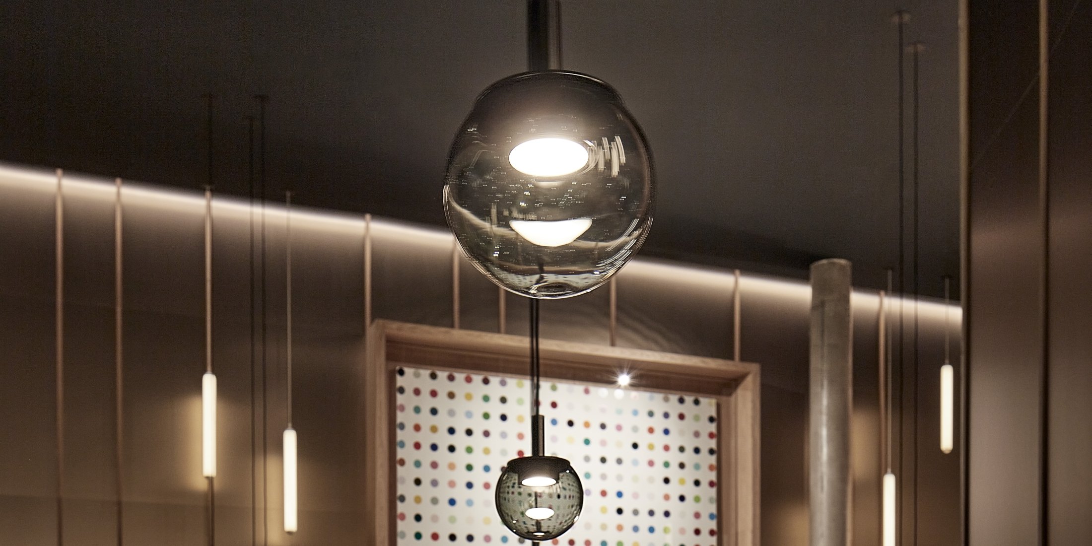 Brokis Orbis pendants glows above with a reflective orb, with vibrant dot art accenting a rich brown wall.