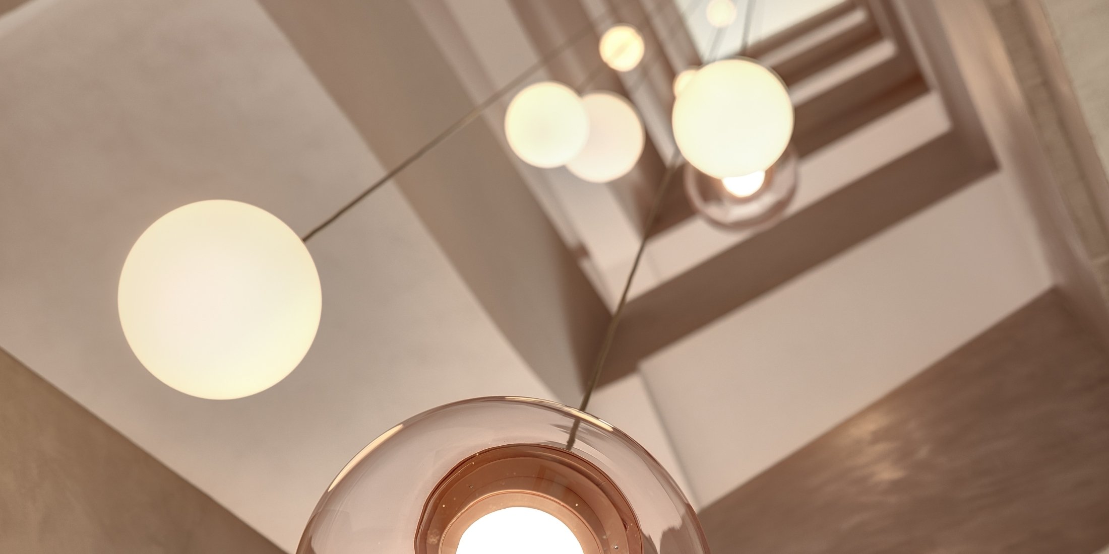 Brokis Sfera pendants with an upward view of a modern staircase, with glass spheres glowing along sleek geometric lines.