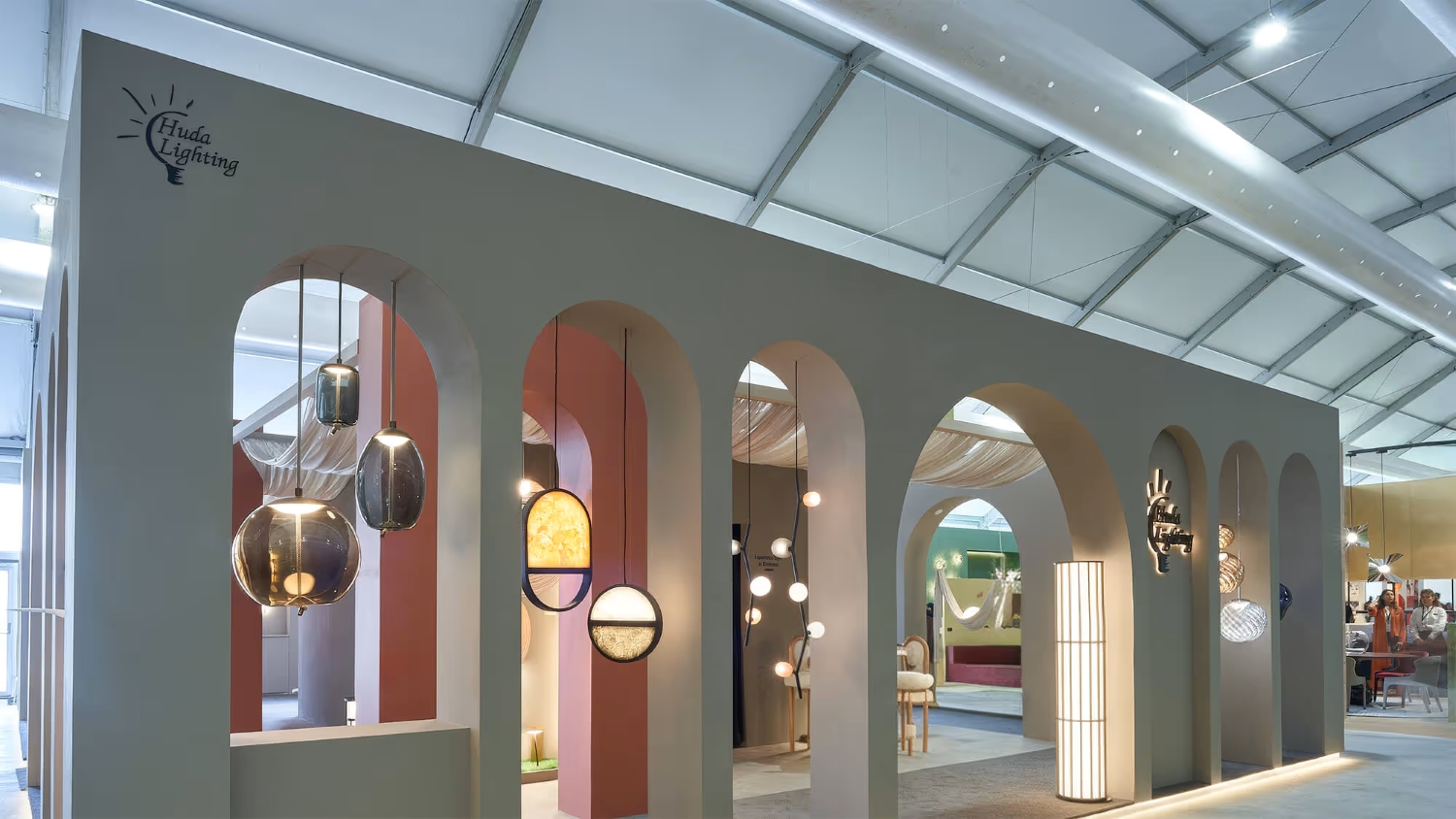 A luxurious stand with arched entrances displays Brokis lighting beneath draped ivory fabric and ambient walls.