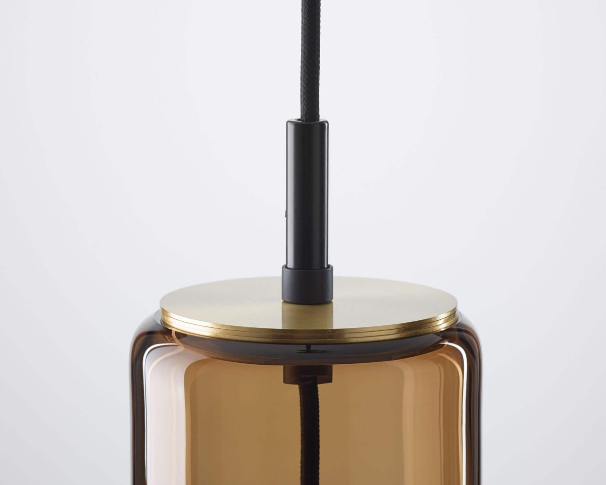 Brokis pendant solution with handblown brown glass cylinder with brass cap and black cord, on white backdrop.