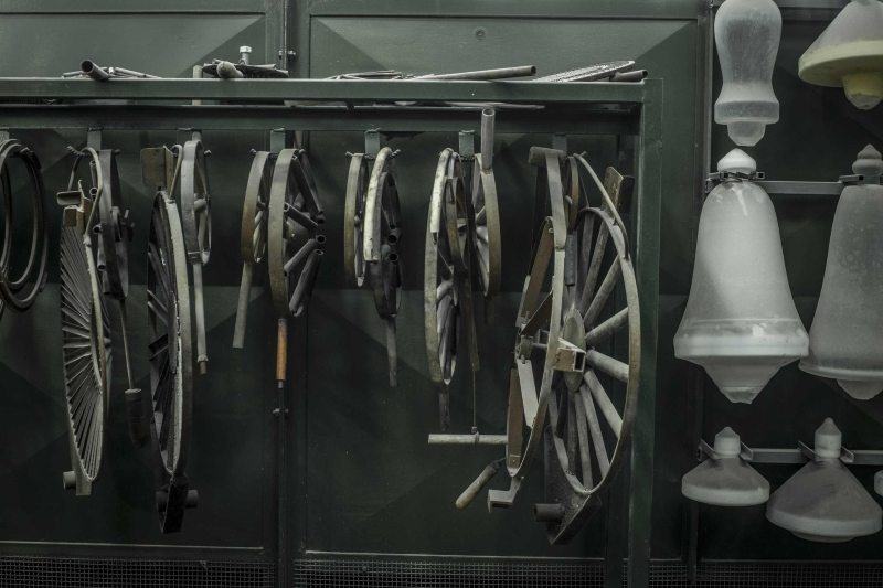 Metal wagon wheels and circular frames hang on a dark green wall; handblown Brokis glass shade covers are suspended nearby.