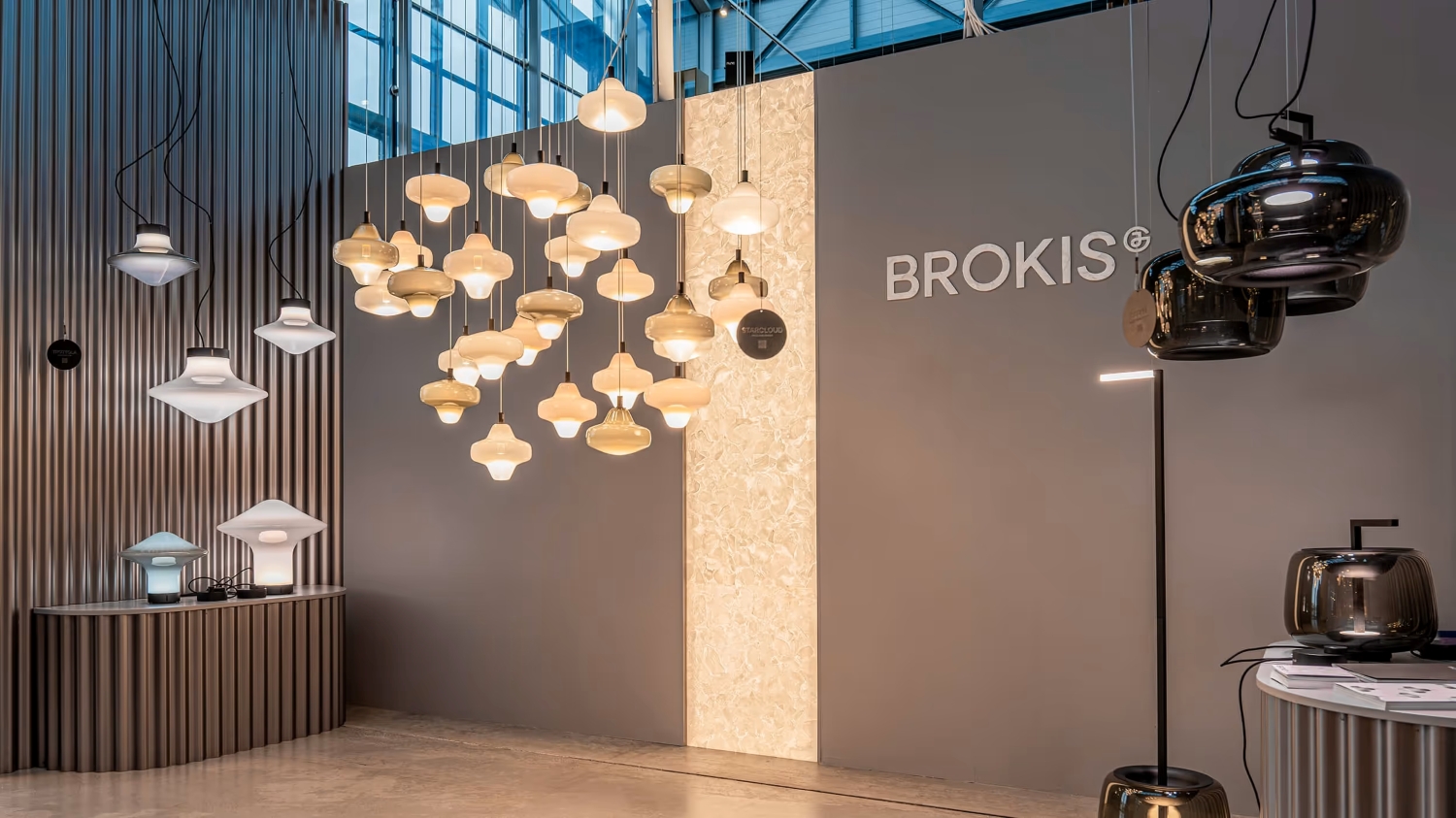 A modern showroom features Brokis Starcloud pendants in clusters, glowing against a stone-lit grey wall.