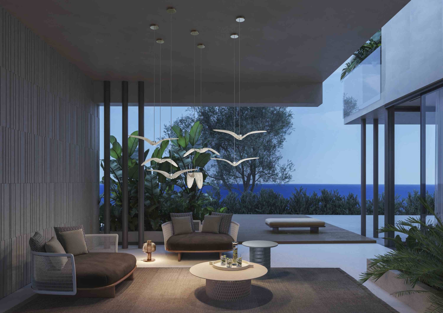 Chic outdoor lounge with dark cushioned sofas, Night Birds Exterior pendants, sea views, and lush greenery.