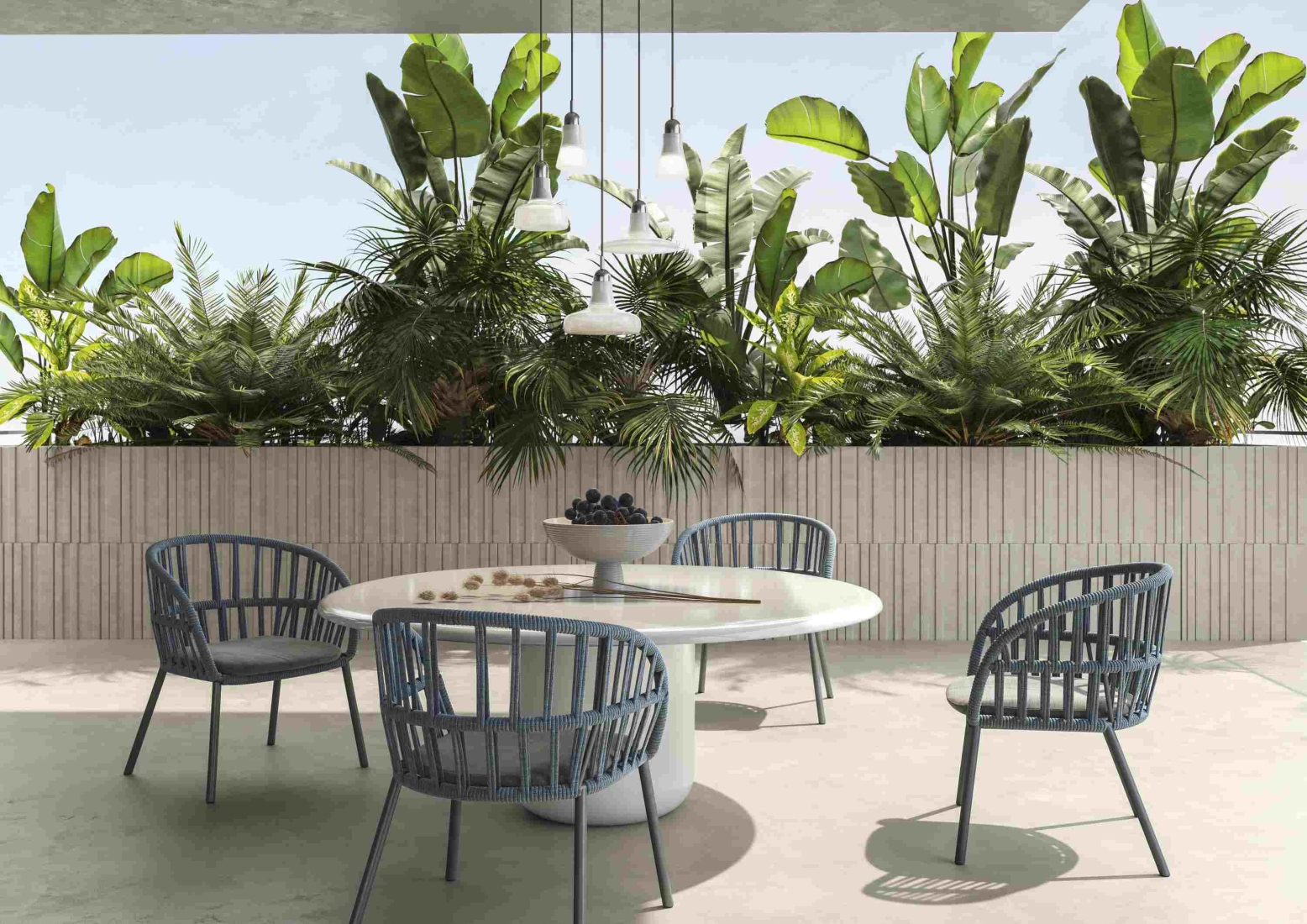 A round white table with grapes, four dark blue chairs, lush patio greenery, Brokis Shadows Exterior pendants above.