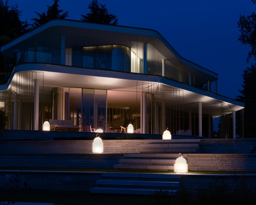 A modern two-storey house with large glass windows is aglow, Brokis Dome Nomad lights accenting its sleek stone steps.