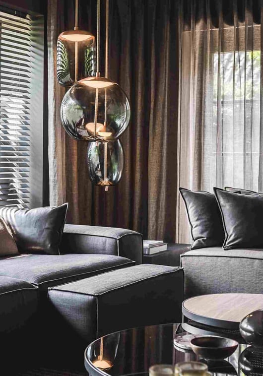 Sophisticated living room with grey sofas, dark cushions, a glass coffee table, Brokis Knot pendants.