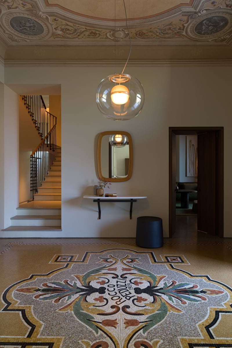 Brokis Big One Large pendant in a corridor with a vibrant mosaic floral floor, console and mirror, and dramatic stair.