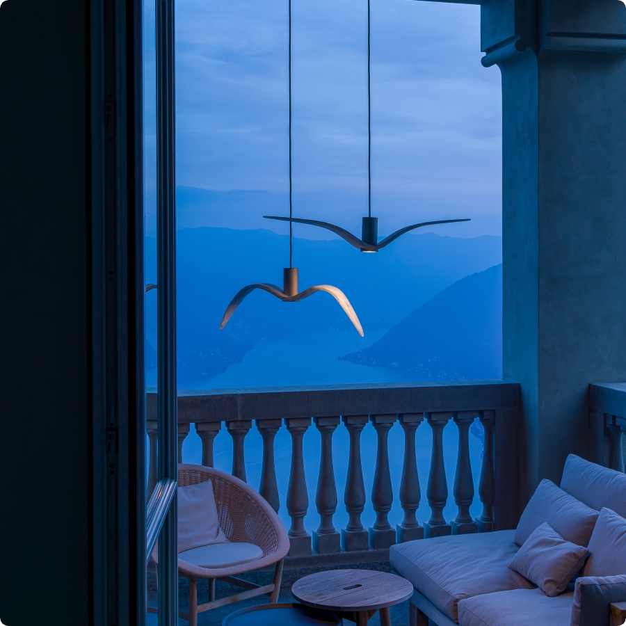 Brokis Night Birds above elegant seating, in a balcony at dusk, with a lake and mountain views beyond.