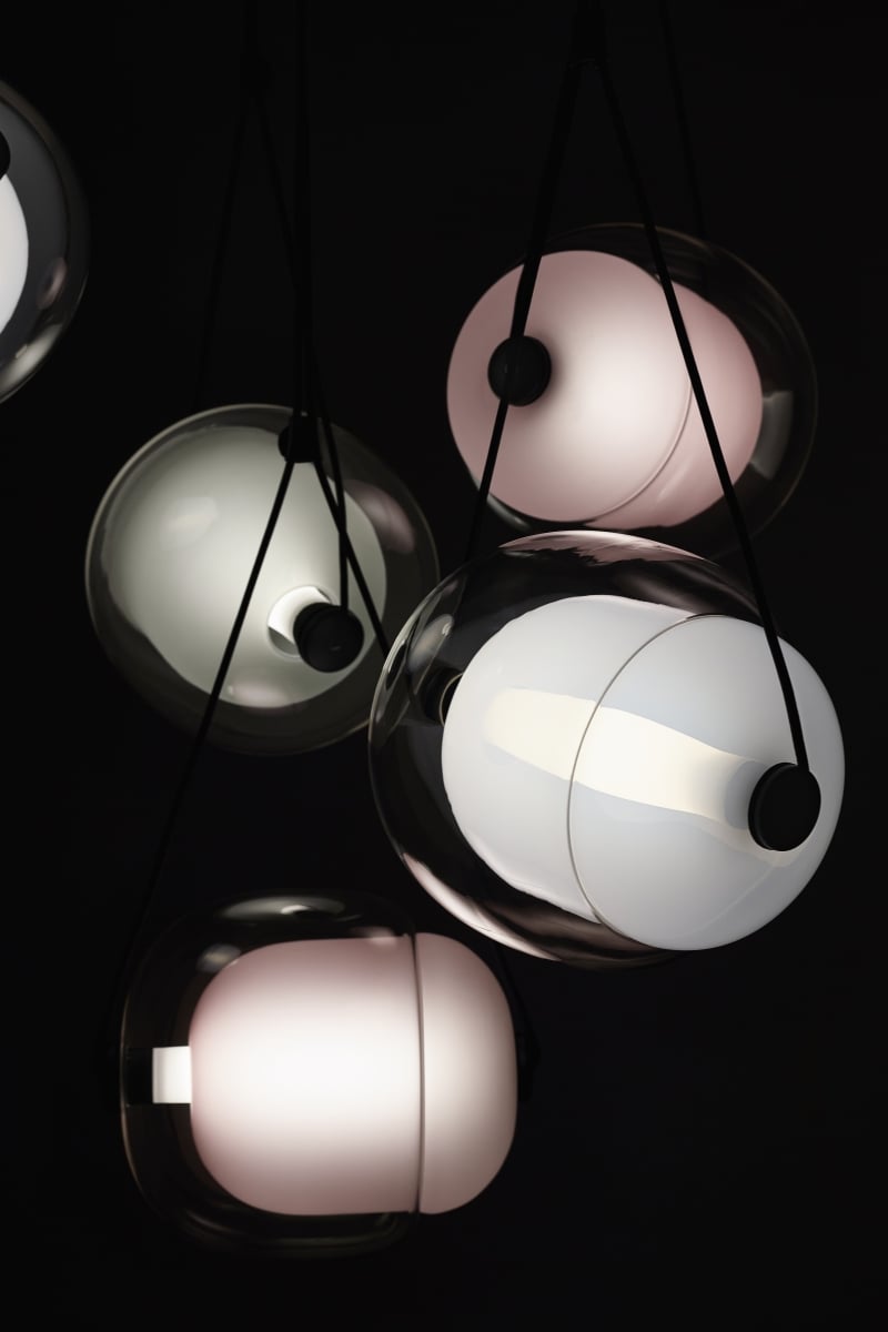 Brokis Capsula pendants with rounded glass shades emit a soft glow, exuding modern luxury against a dark backdrop.