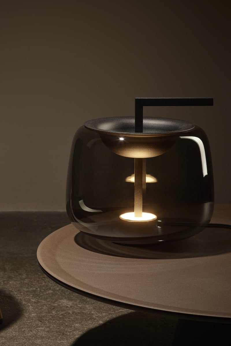 Brokis Double Table lamp in handblown glass with a sleek metal rod and circular LED, set on a matt brown surface.