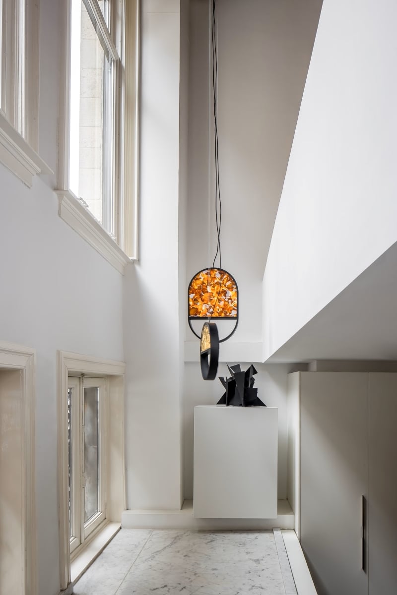 Brokis Geometric pendant in a modern corridor with tall windows, white marble floor, and sleek black art pieces.