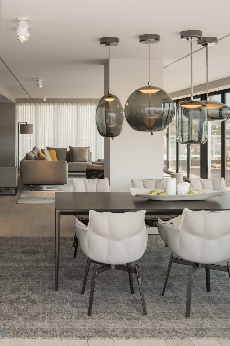 Brokis Knot pendants in a stylish dining area with four white cushioned chairs, and dark table.