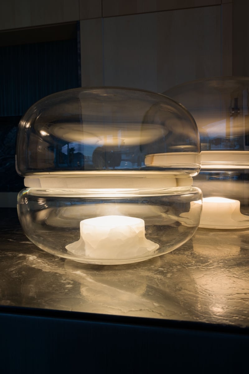 Brokis Macaron S lamp in a handblown glass dome emits a warm glow atop polished dark marble in a luxe interior.
