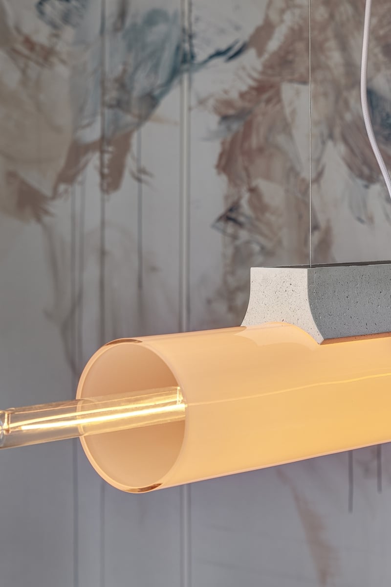 Brokis Overlay L Chandelier with a handblown amber glass shade glows warmly atop a concrete block, against an abstract mural.