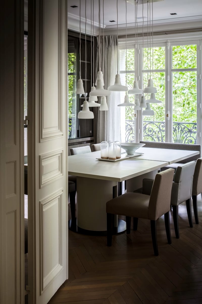 Brokis Shadows pendants in a sophisticated dining room with, modern white table, plush beige chairs, and parquet floors.
