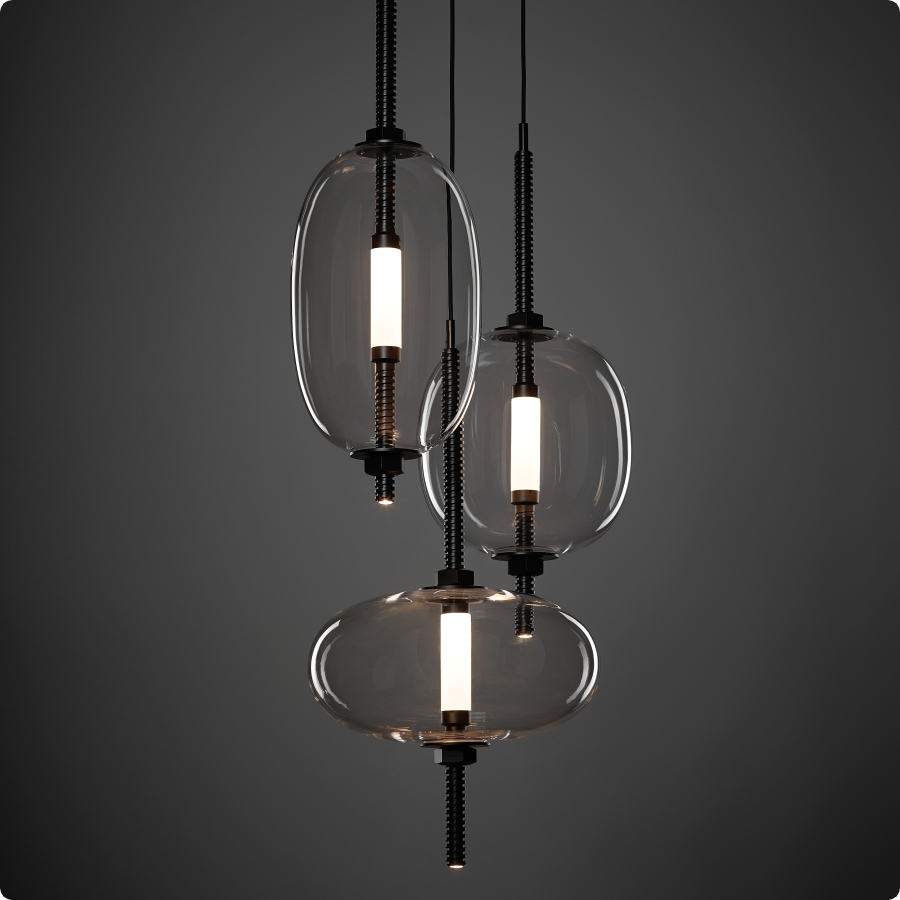 Brokis Under Pressure pendants with handblown glass ovals and elongated LED float at varied heights on a moody grey backdrop.