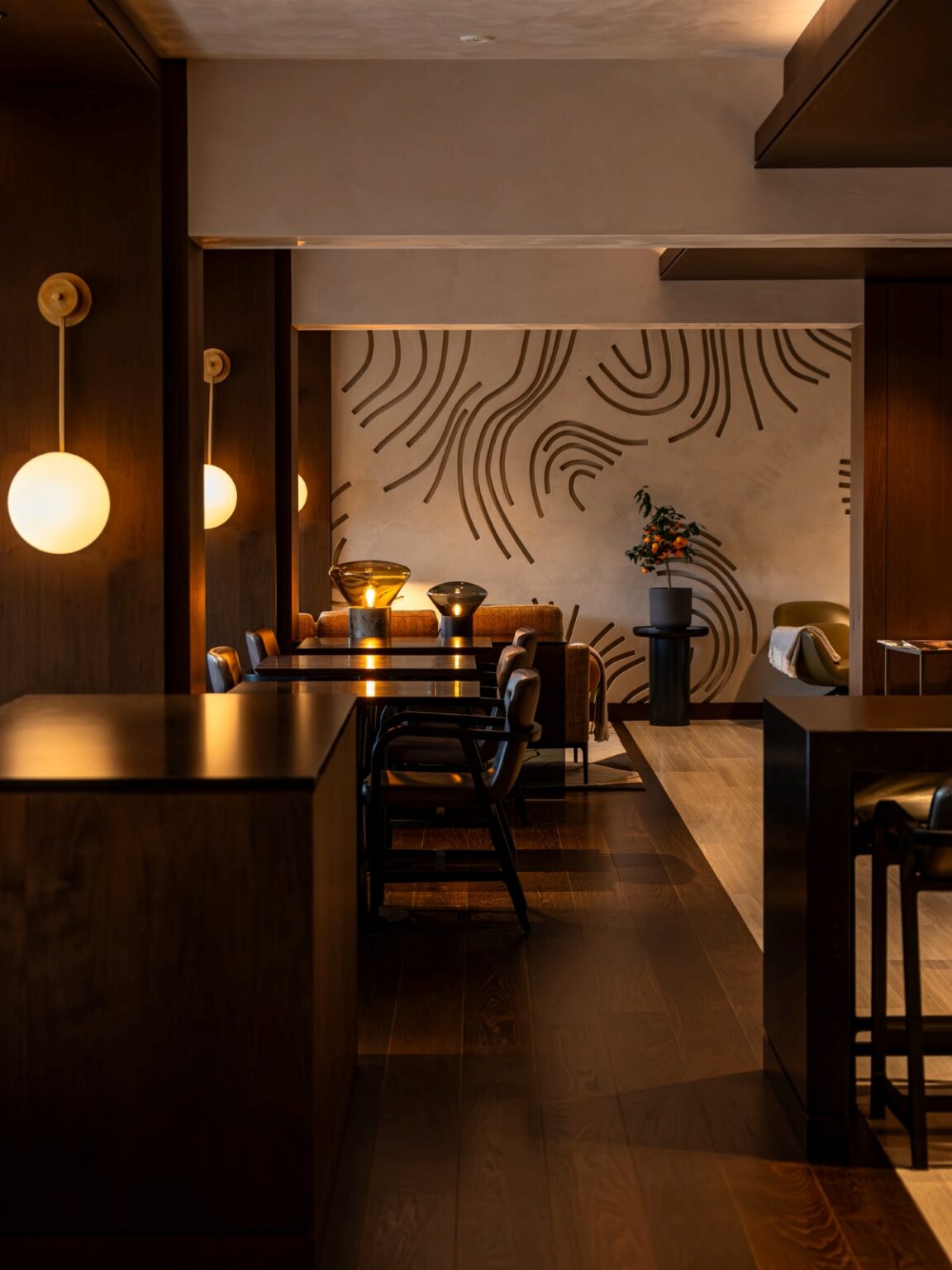 A luxury, warmly lit dining area with dark wood furniture, Brokis Muffins Table lamps wavy art, and elegant floral accents.