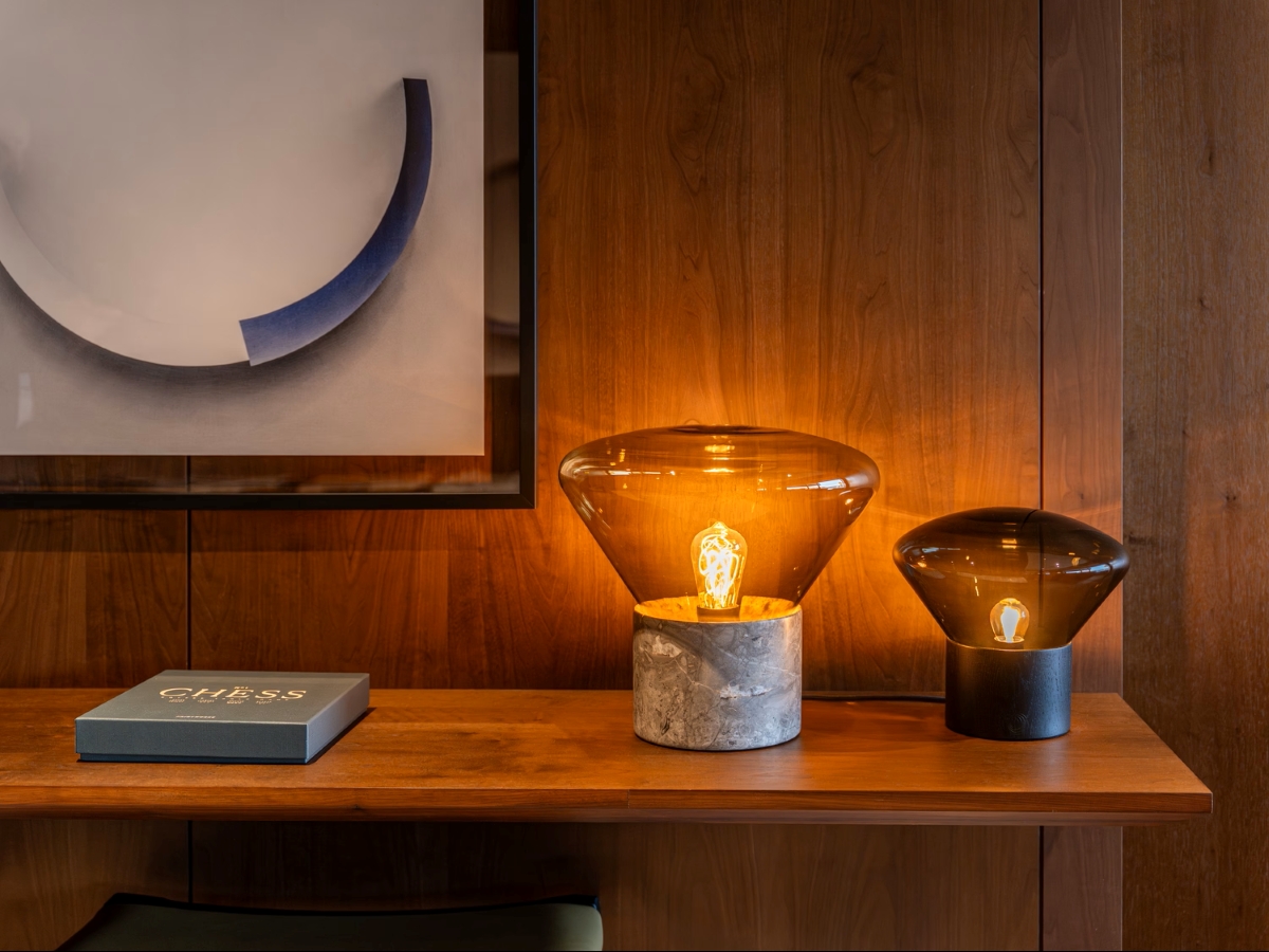 A wooden shelf displays Brokis Muffins table lamps with exposed bulbs on marble and black bases, beside a blue chess box.