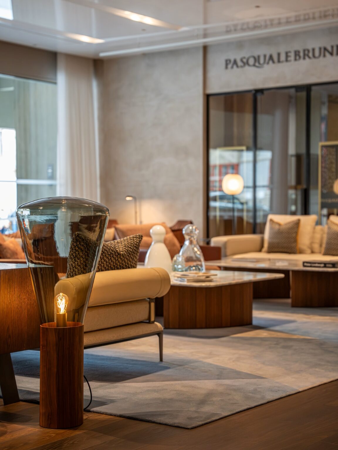 A refined lounge with beige sofas, wooden tables, luxe cushions, blue-grey rug, and a Brokis Muffins floor lamp on display.