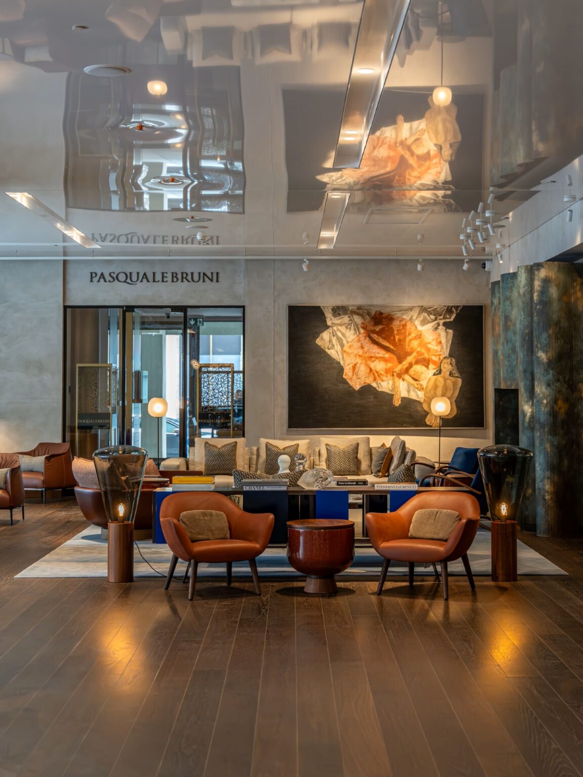 A luxurious lounge with brown leather chairs, a glass table, beige sofa, abstract art, and Brokis Muffins floor lamps.