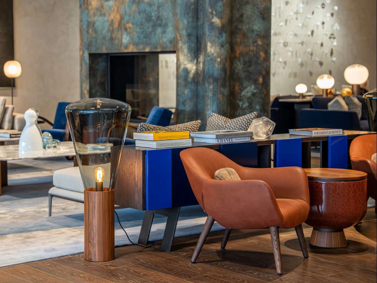 Sophisticated lounge with brown leather armchairs, blue bookcase, round table, Brokis Muffins floor lamp, and plush sofas.